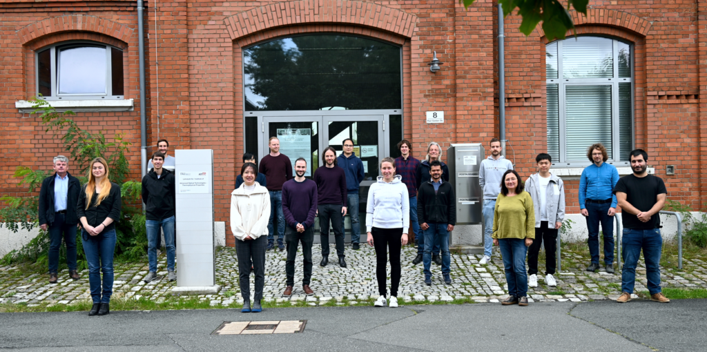 Photograph of AOT-TP team in September 2022; the group members are standing with adequate mutual distance in front of the entrance door of the institute
